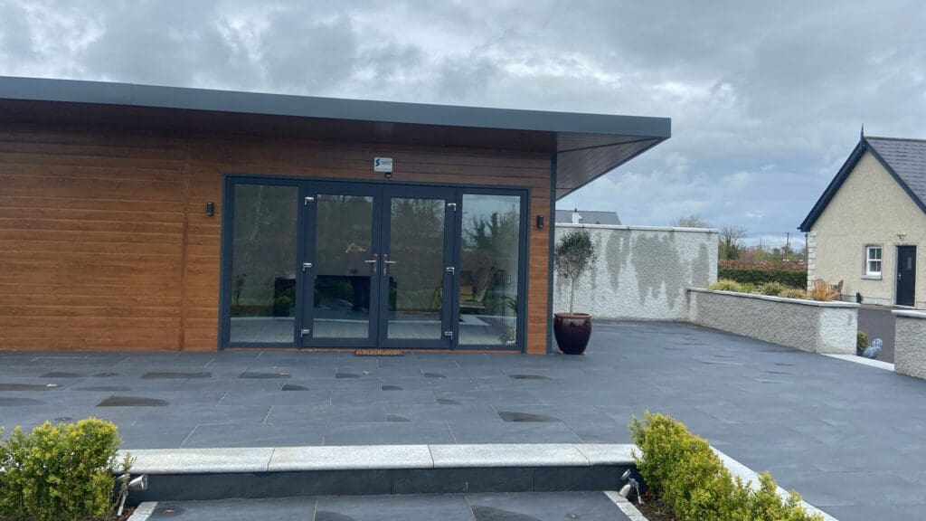8 m × 5 m insulated steel garden room clad in golden oak composite panels with floor-to-ceiling glazing