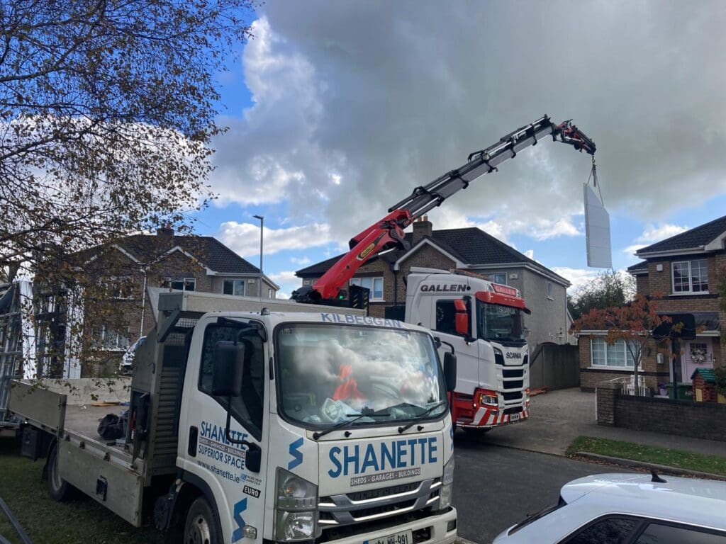 Crane lifting house extension composite panels above an existing home roof by Shanette Sheds