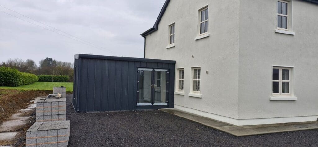 Rear view of a standing-seam home extension with dark-grey metal cladding and full-height patio doors.